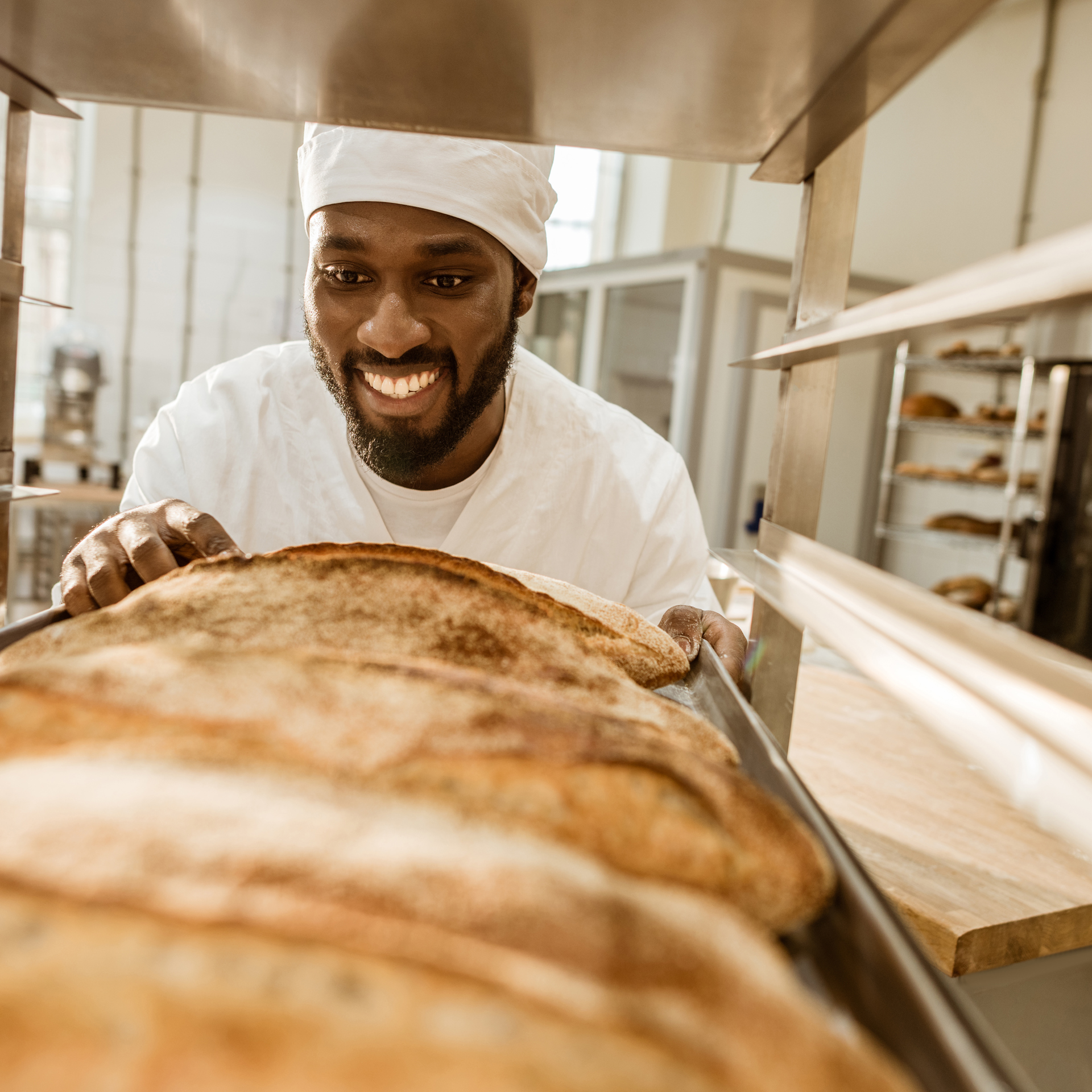 26163851 Smiling African American Baker Looking At Fresh Loaves Of